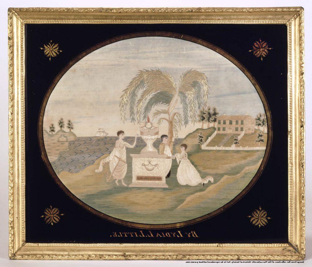 A color photograph of a framed embroidered cloth in an oval shape with black filling in from the oval to the frame. The image is of three children surrounding an urn on a gravestone with a weeping willow behind them, a house in the background and a ship in a harbor on the other side. 